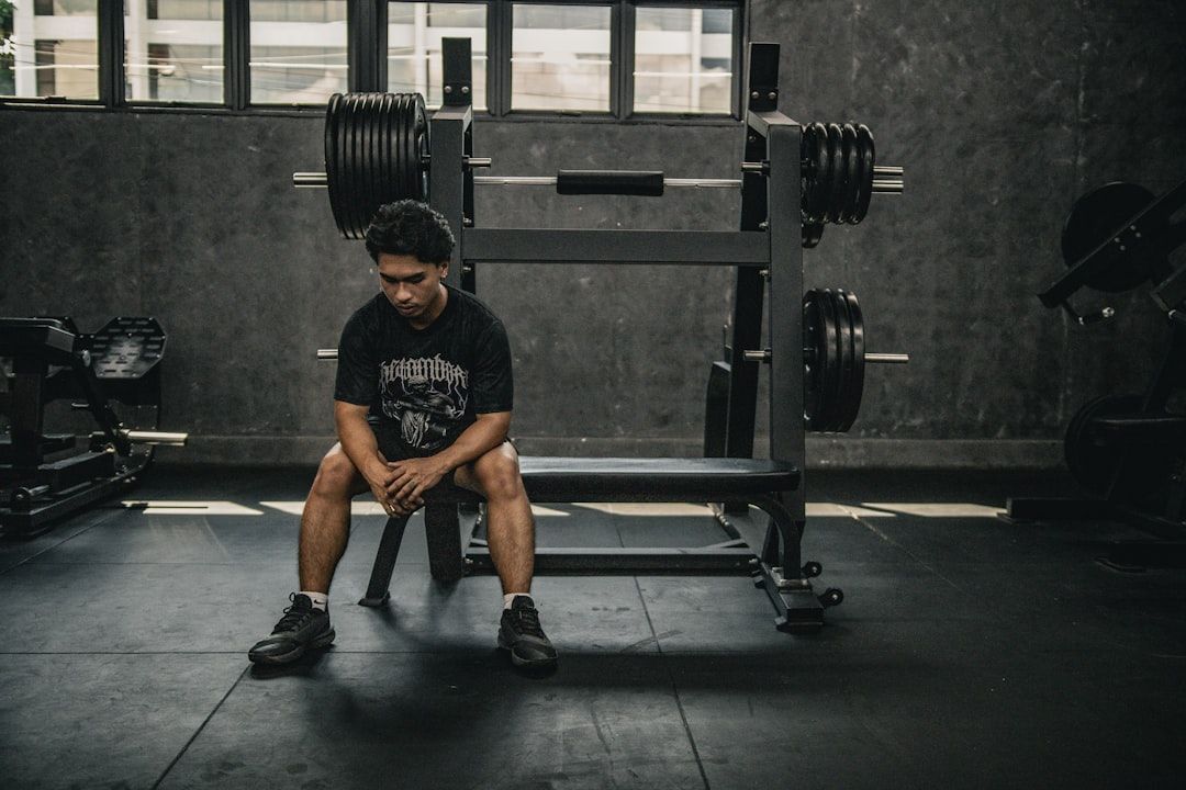 Man sitter på en bänk framför en robust skivstångsställning i ett gym.