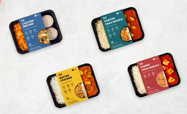 Färdigförpackade indiska maträtter i svarta plastbehållare på en ljus yta.