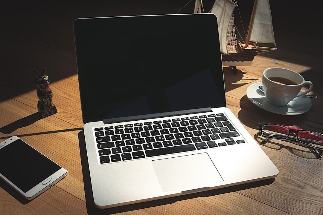 Laptop på ett träbord med telefon, kaffekopp och glasögon